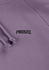 Fioletowa bluza polarowa o miękkiej fakturze z zawiązanym sznurkiem. Na przodzie znajduje się czarne haftowane logo "PROSTO."