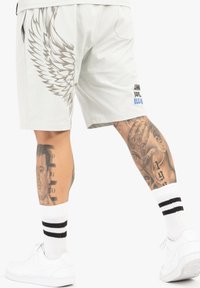 Heledad hallid lühikesed püksid, mille vasakul küljel on tiiva graafika, taskud ja sinine tekstilogo. Kanna valgete sokkide ja tossudega.