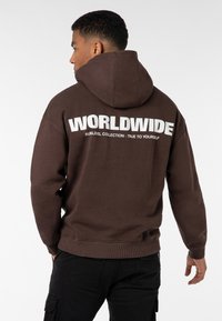 Brauner Hoodie mit Kapuze, auf der Rückseite mit großen weißen Buchstaben bedruckt, die "WORLDWIDE" und "SUBLEVEL COLLECTION - TRUE TO YOURSELF" lesen.