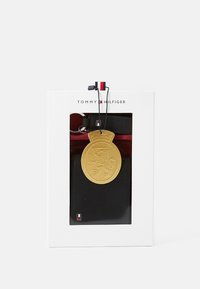 Porte-clés portefeuille noir avec une finition texturée, doté d'une médaille dorée avec un design de lion, attachée par un cordon noir. Emballé dans une boîte blanche.
