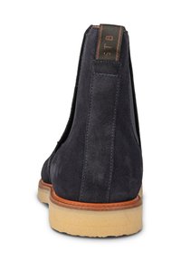 Navy blue mokkasiner med strukturerad finish, elastiska sidopaneler och en ljusbrun sula med subtila spårdetaljer.