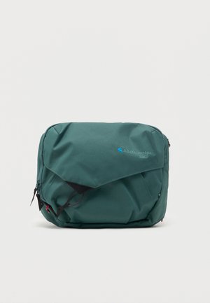 Borsetă verde din material textil, cu buzunar frontal cu clapetă prevăzut cu fermoar, detalii negre cu șnur și un mic logo albastru pe față.