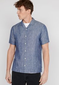 Camicia a maniche corte con bottoni in un tessuto gradient blu texture. Presenta un colletto da campeggio e bottoni di colore chiaro per contrasto.