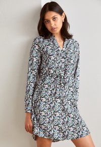 Blommig klänning med svart bakgrund, med långa ärmar, v-ringning och åtsittande midja. Små, färgglada blommönster över hela.