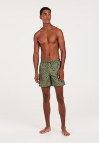 Zielone kąpielówki z czarnym abstrakcyjnym wzorem, z regulowanym pasem i logo na brzegu. Gładki materiał i długość do kolan.