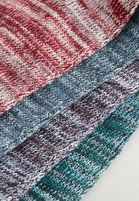 Prim-plan cu mostre de țesătură tricotată pliate, în roșu, albastru, mov și verde, cu fire albe împletite care creează un model în dungi.