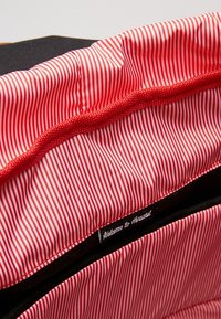 Doublure rayée rouge et blanche avec un fini texturé, comportant une poche noire et une étiquette "Bienvenue chez Herschel" cousue en blanc.