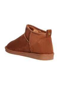 Botas de tobillo de ante marrón con un suave forro de piel, diseño de perfil bajo y suela de goma texturizada. Presentan un emblema circular en la parte trasera.