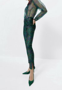 Ohut kukkakuosiset blouse sinisenä ja vihreänä, istuvat kukkakuosiset housut sivurei'illä, yhdistettynä vihreisiin lakatusta nahasta tehtyihin korkokenkiin.