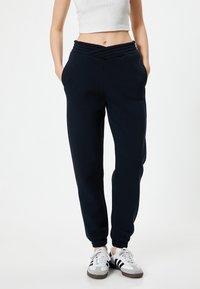 Marineblauwe sweatpants met een Gathered tailleband, taps toelopende pijpen en zijzakken, gecombineerd met witte en zwarte sportschoenen.