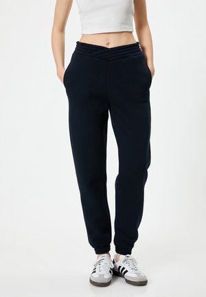 Navy blue sweatpants with a gathered waistband, tapered legs, and side pockets, paired with white and black athletic sneakers.