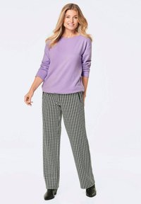 Hellblauer Pullover mit langen Ärmeln, kombiniert mit einer Hose im schwarz-weißen Hahnentrittmuster. Model trägt schwarze Stiefeletten.