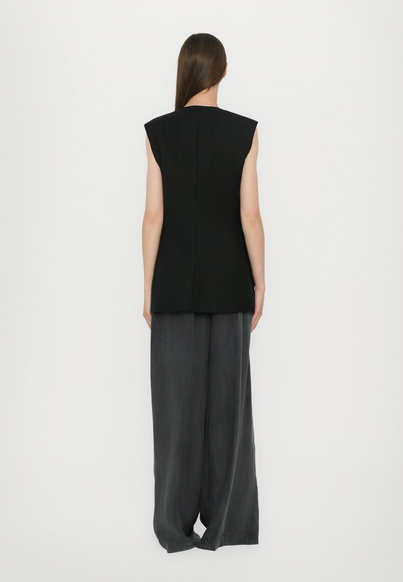 Black sleeveless top with shoulder accents and a straight cut, paired with dark gray wide-leg trousers. Smooth, textured fabric.