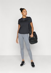 Μαύρο κοντομάνικο t-shirt με το λογότυπο της Nike, γκρι κολάν και μαύρα αθλητικά παπούτσια. Φοράει μαύρη τσάντα γυμναστηρίου με ιμάντα. Απλός σχεδιασμός.