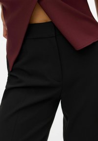 Top bordeaux con schiena aperta, abbinato a pantaloni neri su misura. Tessuto morbido con tasche e taglio dritto sui pantaloni.