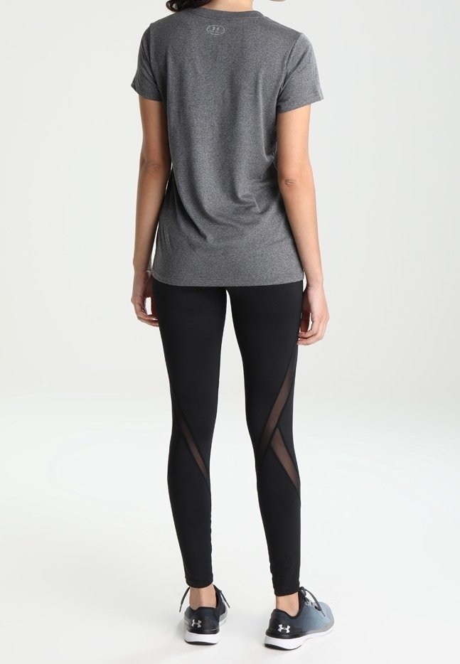 Grå kortärmad träningsskjorta i kombination med svarta leggings med genomskinliga sidopaneler, kompletterat med mörka träningsskor.