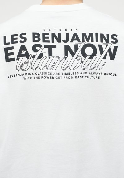 Πίσω μέρος λευκού πουκαμίσου με μαύρο κείμενο: «LES BENJAMINS EAST NOW Istanbul» και μικρότερο κείμενο για τον διαχρονικό, μοναδικό πολιτισμό της Ανατολής.