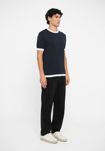 T-shirt de manga curta numa cor azul marinho com decote e punhos canelados brancos, combinado com calças pretas e ténis de cor off-white.