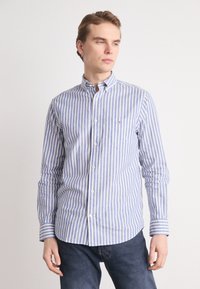 Camisa de botones a rayas azul y blanca, de manga larga, material de algodón, que presenta un bolsillo y un pequeño logo en el pecho.