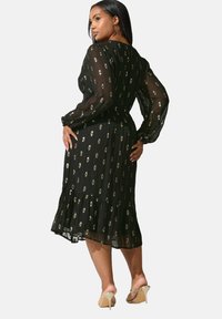 Svart, blommönstrad midiklänning med långa, genomskinliga ärmar och volangkant. Tillverkad av lättviktig tyg och med en figurnära midja.