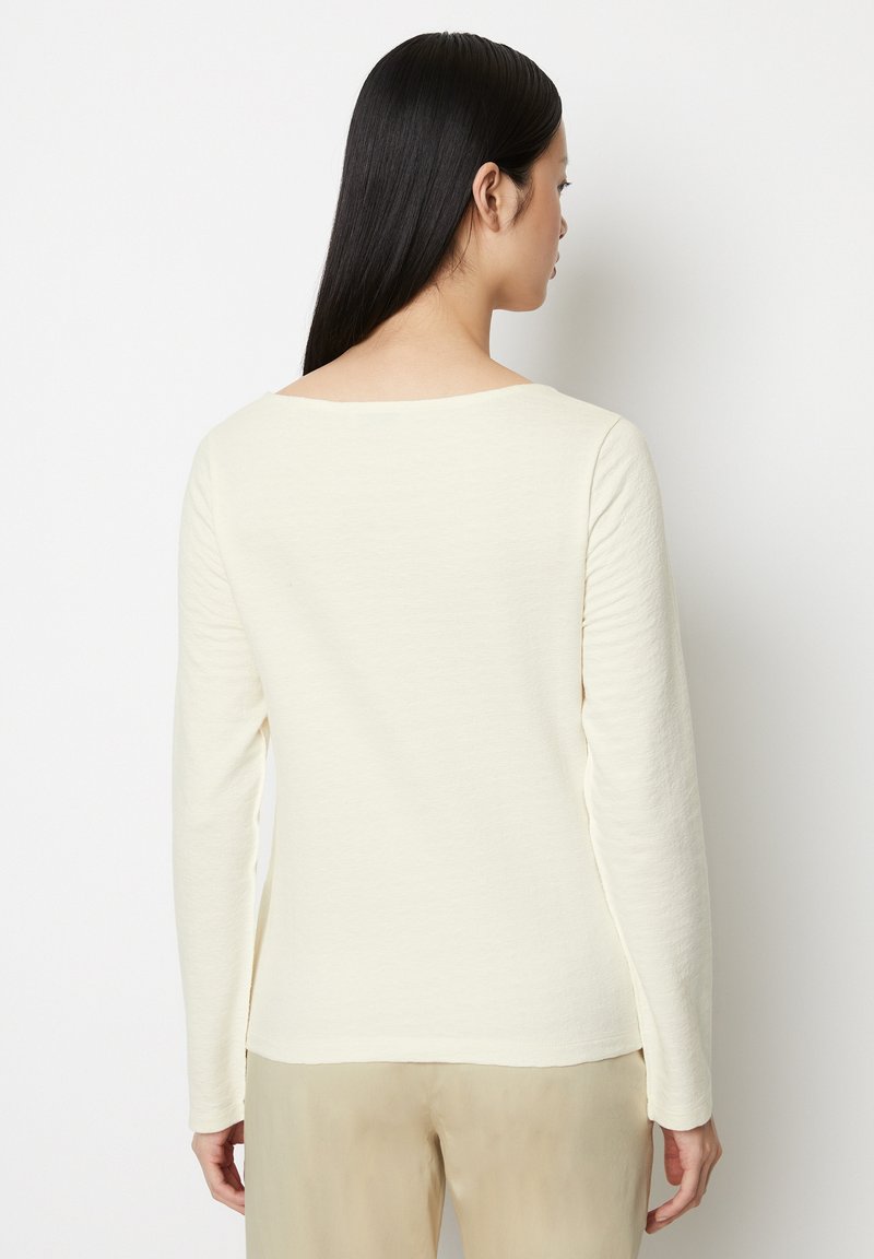 Crème lange mouwen top met een brede halslijn, zachte textuurstof en een rechte pasvorm, gecombineerd met lichtbeige broeken.