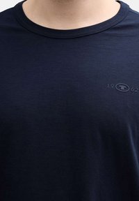 T-shirt bleu marine à col rond, fabriqué dans un tissu lisse. Il présente un petit logo et l'année "1962" brodés sur la poitrine.