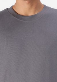 Tricou gri cu mânecă scurtă și decolteu rotund, fabricat dintr-un material de bumbac moale, având o textură netedă și un design discret.