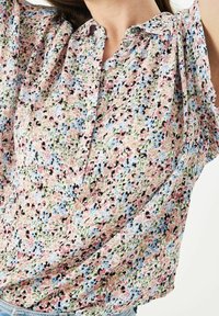 Camicia a maniche corte floreale in tessuto leggero, con motivi in rosa, blu e verde, dotata di patta con bottoni e texture morbida.