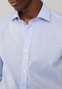 Camisa abotonada azul claro hecha de una tela suave, con un cuello clásico, botones frontales y una textura sutil.