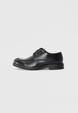 Zapatos de cuero negro con cordones y puntera redondeada, de textura suave y tacón bajo. Presentan detalles de costura a lo largo de la parte superior y los lados.
