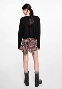 Schwarzer, verkürzter Pullover kombiniert mit einem blumigen, bordeauxroten Minirock, der einen rüschengeschmückten Saum hat. Abgerundet mit kniehohen schwarzen Stiefeln und grauen Socken.