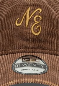 Καφέ καπέλο από κόρντορου με ρυθμιζόμενο λουράκι, διακοσμημένο με χρυσή κεντημένη λογότυπο "NE" και στρογγυλή ετικέτα που αναγράφει "9TWENTY."