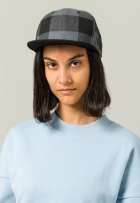 Mustmust ja halli ruuduline beebise hatt, lame äärega, valmistatud tekstuuriga kangast. Kombineeritud helesinise ümar kaelusega sviitriga.