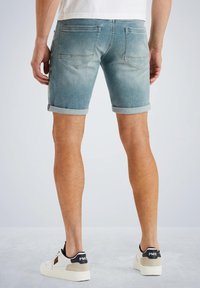 Pantalones cortos de mezclilla en azul claro con dobladillos enrollados, que cuentan con dos bolsillos traseros y un ligero desvanecimiento. Combinados con zapatos blancos y un tacón con detalles en negro.