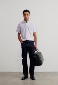 Ανοιχτό μπλε κοντομάνικο πουκάμισο, σκούρο τζιν, μαύρα παπούτσια και μαύρη δερμάτινη τσάντα με ασημένες λεπτομέρειες. Μινιμαλιστικός σχεδιασμός και ουδέτεροι τόνοι.