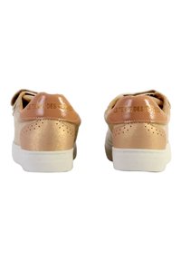 Zapatillas de deporte rosa pálido con un acabado brillante en crema, que cuentan con perforaciones en el talón, suela blanca y un detalle del logotipo en la lengüeta trasera.