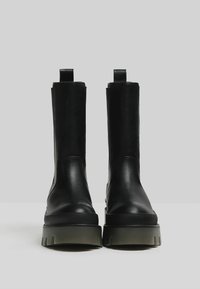 Stivali alla caviglia in pelle nera con finitura liscia, pannelli laterali elastici e suole robuste in gomma verde. Presentano un design a profilo basso con linguette sul tallone.