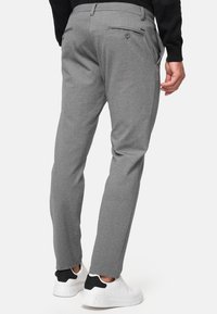 Pantalones grises ajustados con una textura sutil, que presentan bolsillos traseros y un cierre de botón, combinados con zapatillas blancas.