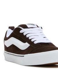 Brune semskete sneakers med hvite detaljer, som har et klassisk bølgedesign, hvite snører og en teksturert gummisåle.