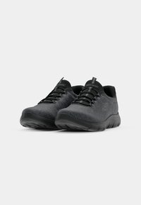 Paire de baskets Skechers gris foncé avec semelles noires et lacets élastiques sur fond gris clair uni.