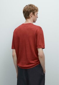 Kr�átký rukáv, tričko s kulatým výstřihem v barvě rezavě červené, vyrobené z texturované látky. Minimální design s žebrovanými detaily na rukávech a lemu.
