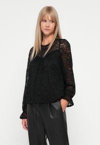 Zwarte kant lange mouwen blouse met een losse pasvorm, voorzien van een ronde halslijn en delicate bloemenpatronen. Draagt met zwarte leren broek.