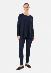 Haut à manches longues bleu marine avec une coupe décontractée et un décolleté arrondi, associé à un jean skinny en denim noir et des ballerines noires. Texture lisse sur l'ensemble.