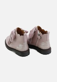 Botas de piel rosa hasta el tobillo con un diseño ondulado, acento plateado brillante en el tacón y grandes lazos de tela en la parte delantera.