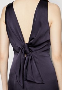 Marinblå satin klänning med djup V-rygg och en rosett som detalj vid midjan. Slät textur med en elegant fall.