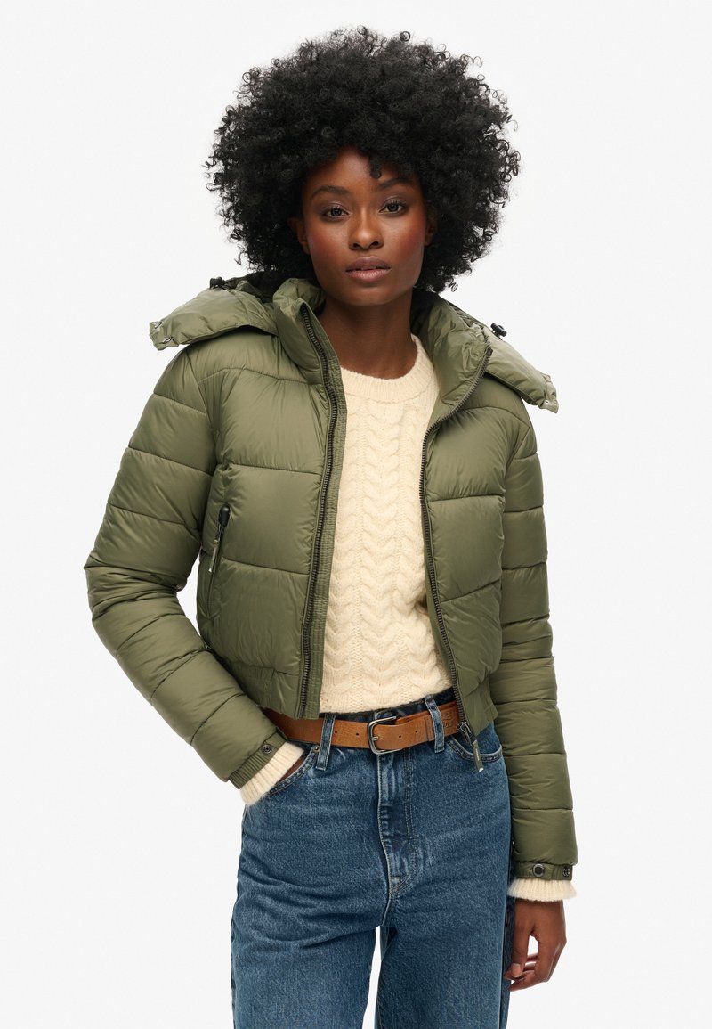 Olijfgroene pufferjack met een cropped ontwerp, voorzien van een capuchon, een ritssluiting aan de voorkant en zijzakken, gecombineerd met een crèmekleurige kabelbrei-sweater.