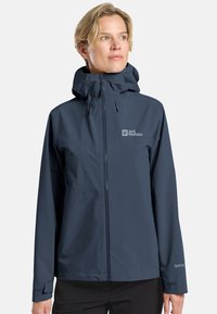 Giacca impermeabile blu navy con zip frontale, cappuccio regolabile e logo visibile. Presenta una texture liscia e polsini elastici.