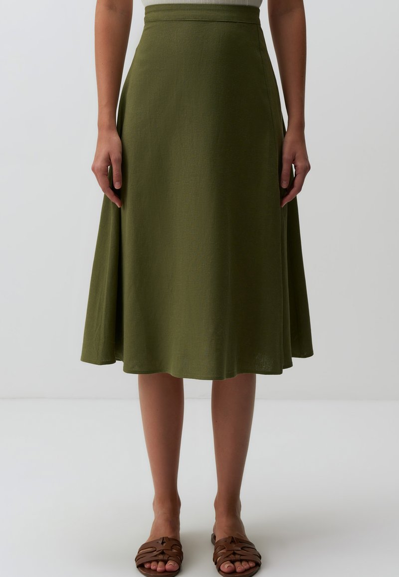 Jupe midi A-line verte en tissu texturé, taille ajustée et ourlet fluide, associée à des sandales plates marron.