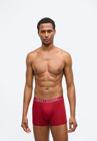 Piros pamut boxer alsónadrág, kontrasztos fehér derékszíjjal, amelyen a "TOMMY HILFIGER" logó található, testhez simuló fazon és sima textúra.