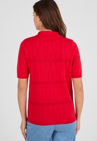Rood poloshirt met korte mouwen, voorzien van een gemêleerd breipatroon en contrasterende horizontale strepen. Het ontwerp van de kraag heeft een klassieke afwerking.